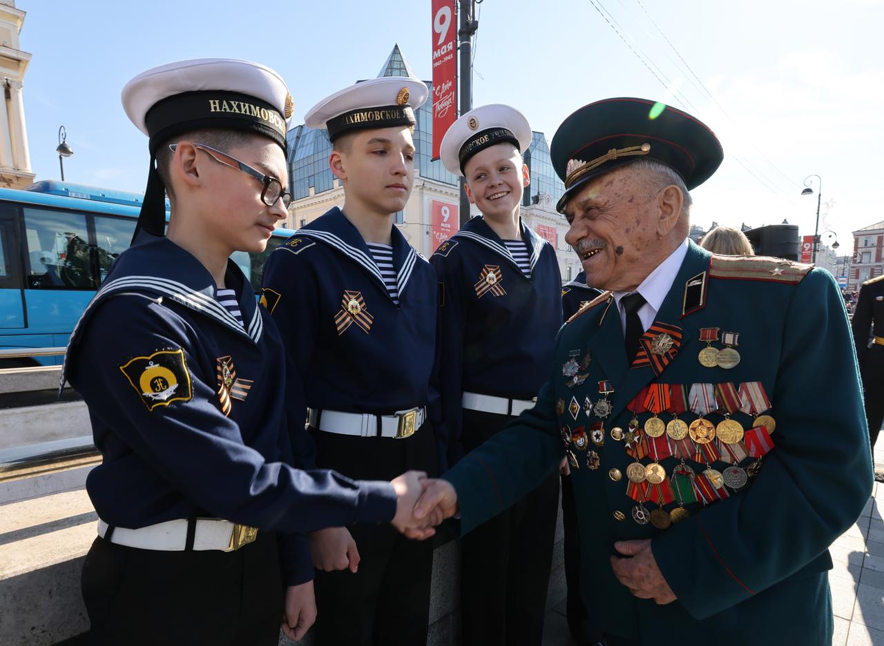 Ein Weltkriegsveteran begrüßt junge rusiche Soldaten.