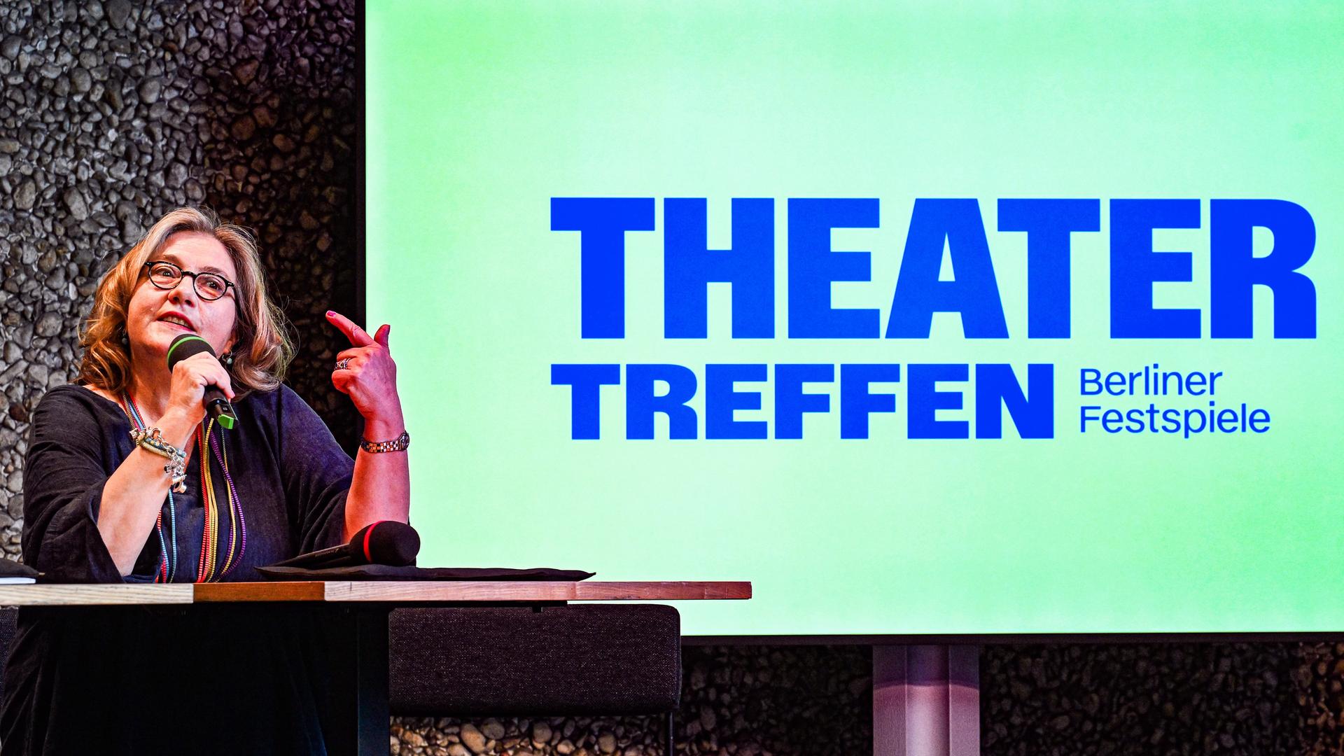 Die Schauspielerin Bettina Stucky bei der Presskonferenz zum Theatertreffen 2025, hinter ihr das Logo des Bühnenfestivals auf grünem Grund. 