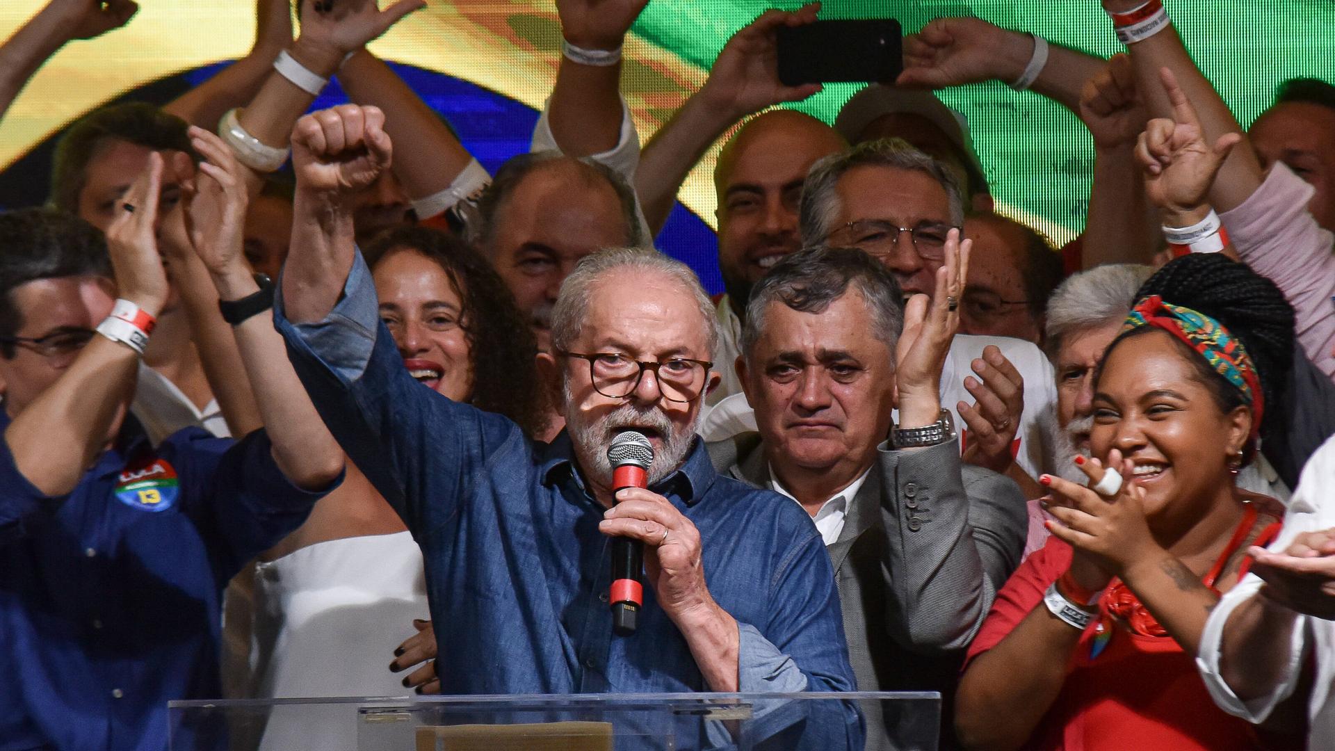 Luiz Inácio Lula da Silva hält eine Rede. Er streckt die Faust in den Himmel. Um ihn herum stehen Anhänger und Anhängerinnen.