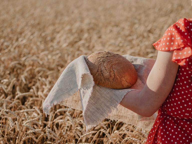Eine junge Frau mit einem Laib Brot in der Hand in einem Getreidefeld
