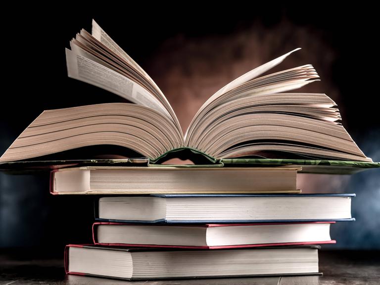 Ein Bücherstapel, das oberste Buch ist aufgeschlagen.