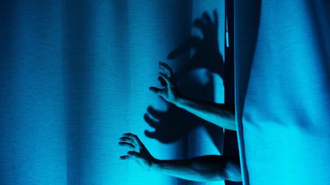 Hände und Schatten greifen durch einen bläulichen Vorhang.