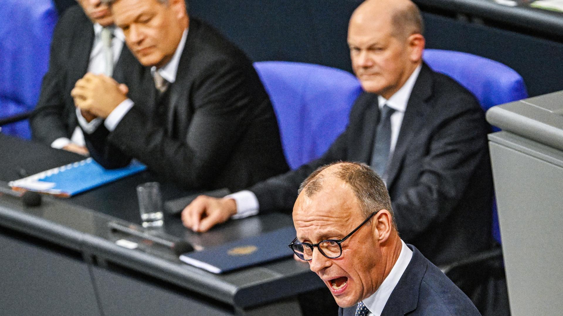 Merz (CDU) am Rednerpult im Bundestag. Dahinter Scholz (SPD) und Habeck (Grüne).