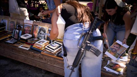 Tel Aviv: Eine Frau trägt ein M-16-Gewehr und platziert Fotos von Israelis, die bei dem tödlichen Hamas-Angriff auf Israel am 7. Oktober 2023 getötet wurden, bei einer Gedenkfeier zum zweijährigen Jahrestag des Angriffs.