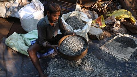 Ein Inder sitzt auf dem Boden, er arbeitet in einer Recycling-Altmetallwerkstatt in Kalkutta, Indien.