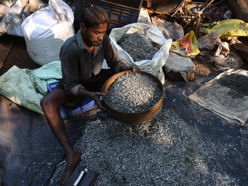 Ein Inder sitzt auf dem Boden, er arbeitet in einer Recycling-Altmetallwerkstatt in Kalkutta, Indien.