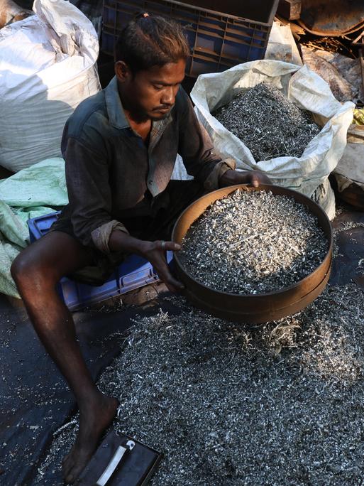 Ein Inder sitzt auf dem Boden, er arbeitet in einer Recycling-Altmetallwerkstatt in Kalkutta, Indien.