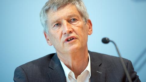 Wolfram König spricht in ein Mikrofon. Er trägt einen dunkelgrauen Anzug und weißes Hemd.