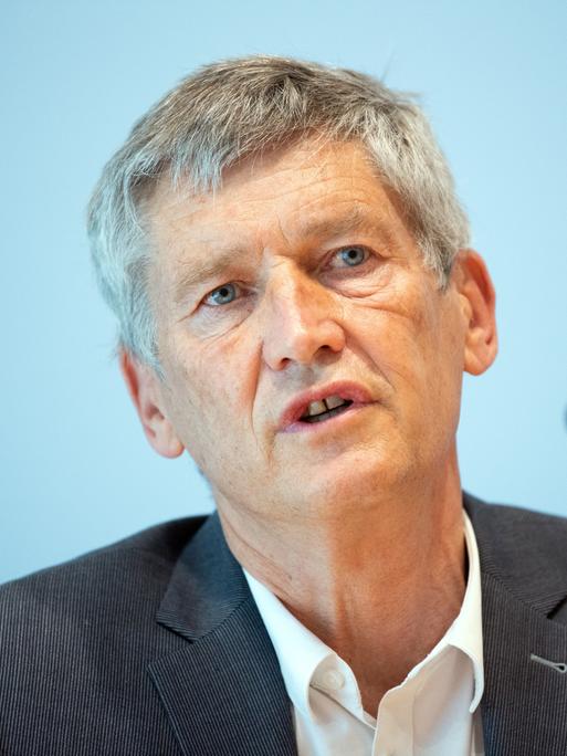 Wolfram König spricht in ein Mikrofon. Er trägt einen dunkelgrauen Anzug und weißes Hemd.
