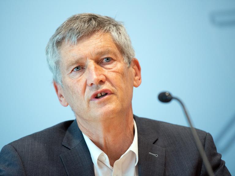 Wolfram König spricht in ein Mikrofon. Er trägt einen dunkelgrauen Anzug und weißes Hemd.