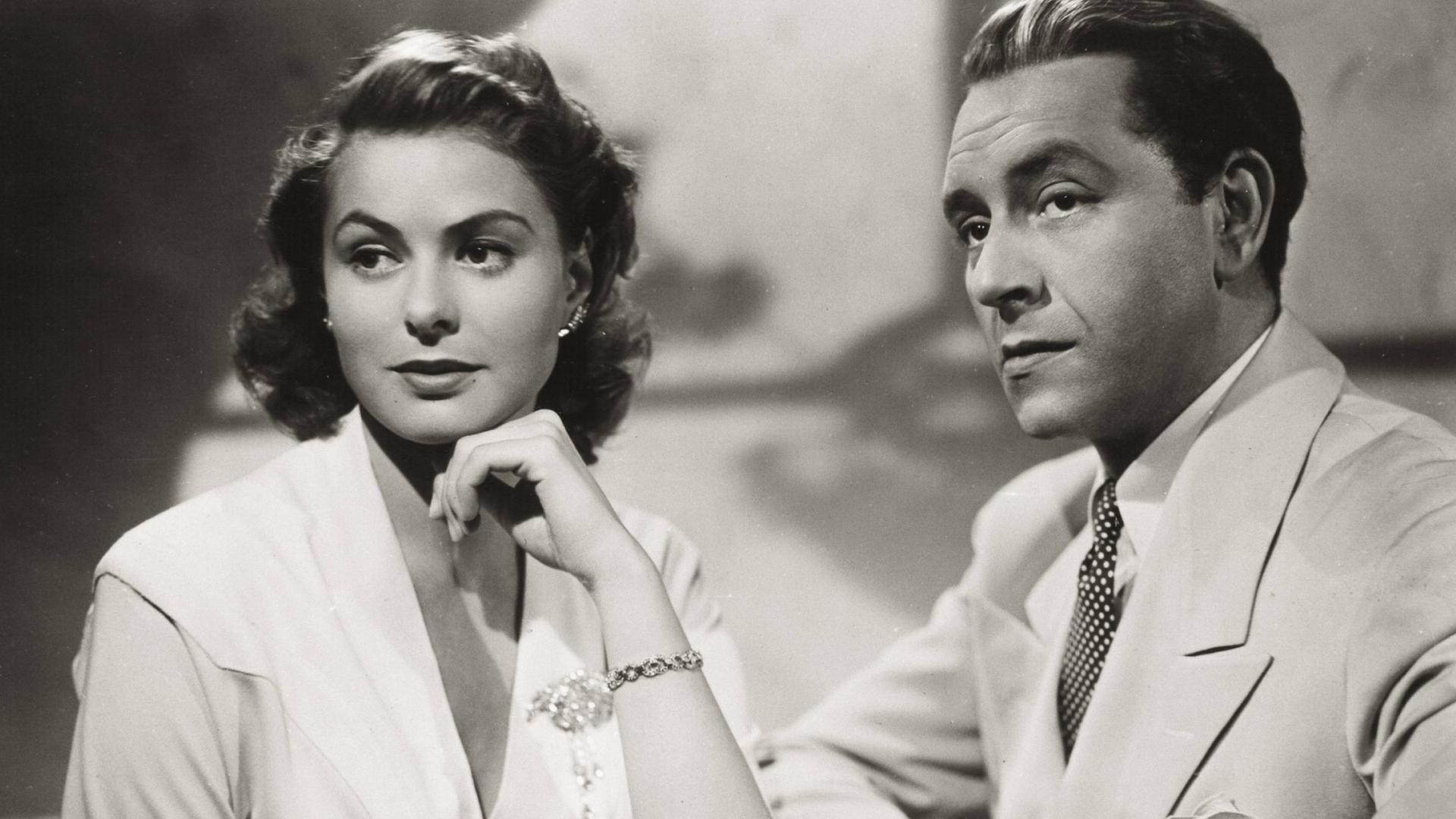 Historisches Schwarzweißfoto von Ingrid Bergman und Paul Henreid, die mit ernstem Blick nebeneinander sitzen.
