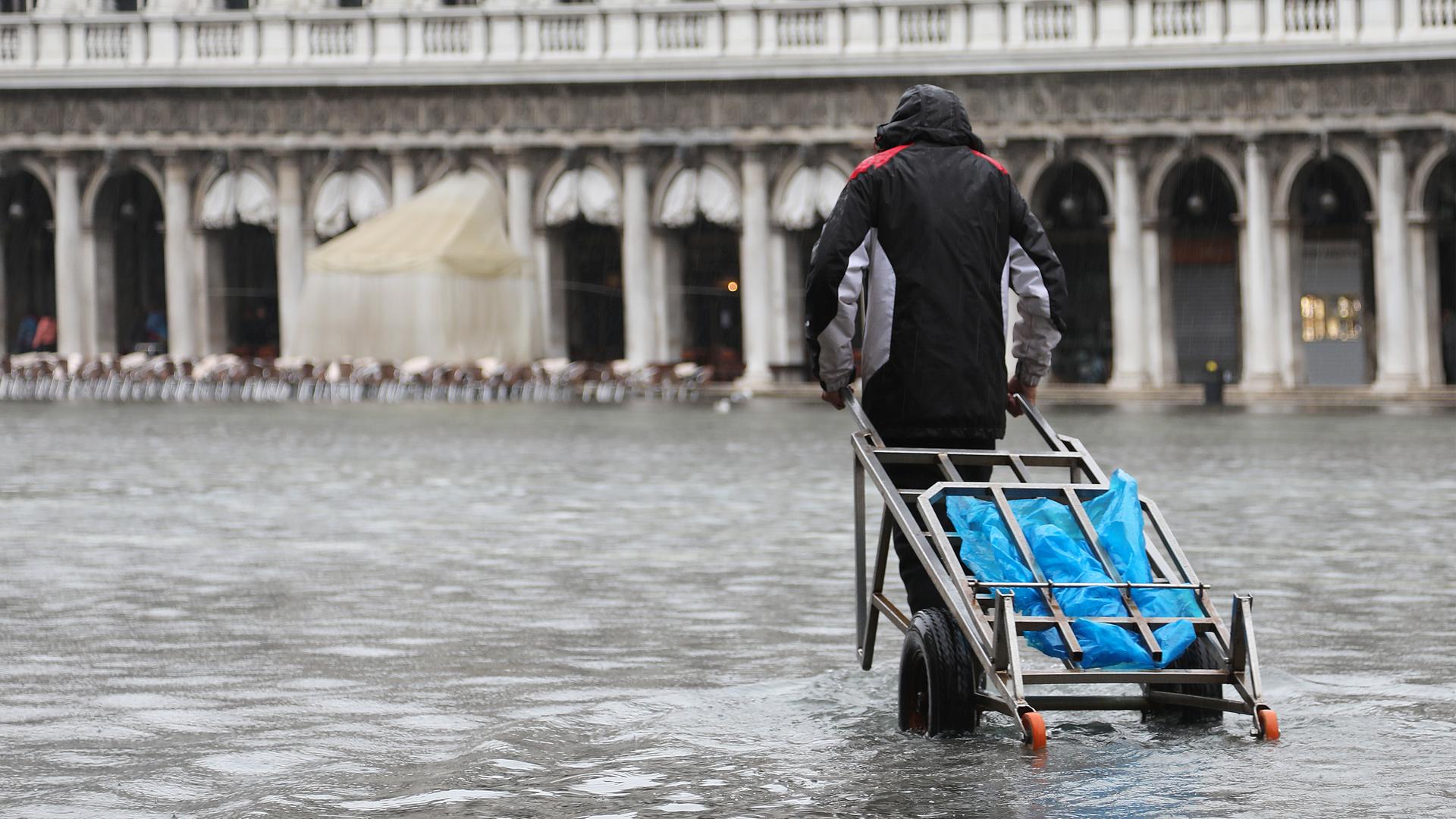 Mann mit Sackkarre geht durch eine überschwemmte Straße in Venedig