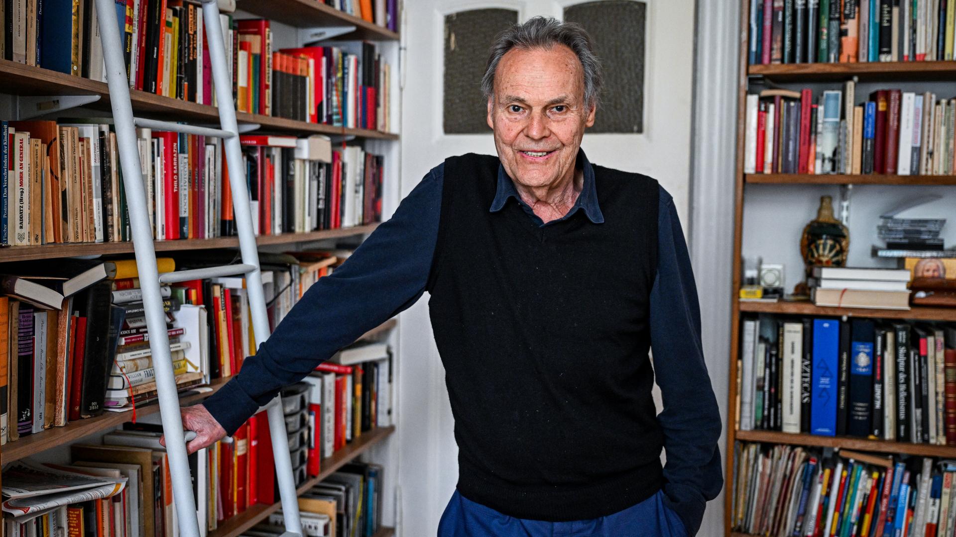 Der Schriftsteller Peter Schneider steht vor einem Bücherregal und lächelt. Der Schriftsteller Peter Schneider steht vor einem Bücherregal und lächelt.