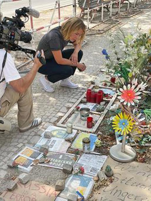 Bild aus der ARD-Reportage von Jessy Wellmer "Russland, Putin und wir Ostdeutsche", darauf ist die Reporterin zu sehen, wie sie an einem Gedenkort für die Opfer des Ukraine-Überfalls durch Russland kniet.