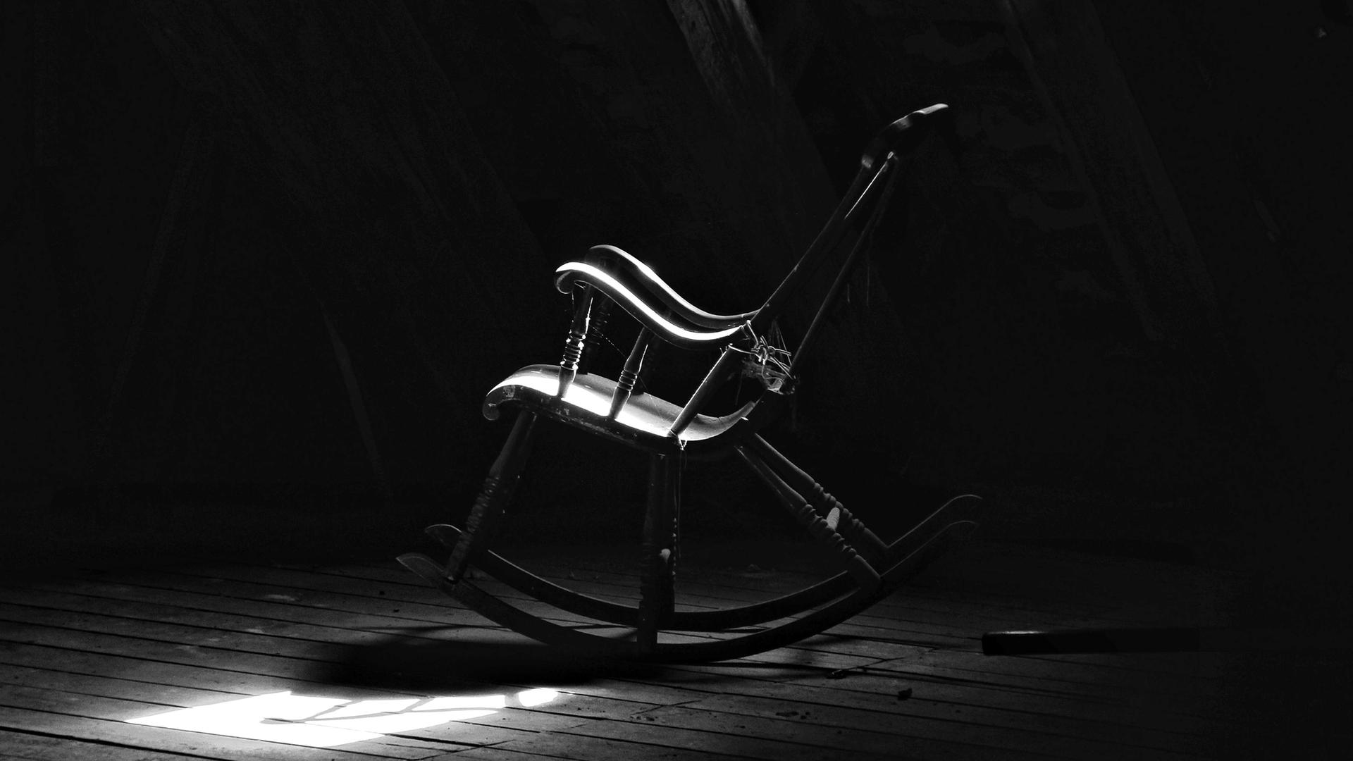 Schwarz-Weiß-Bild eines verstaubten Schaukelstuhls auf einem Dachboden.