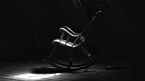 Schwarz-Weiß-Bild eines verstaubten Schaukelstuhls auf einem Dachboden.