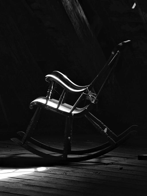 Schwarz-Weiß-Bild eines verstaubten Schaukelstuhls auf einem Dachboden.