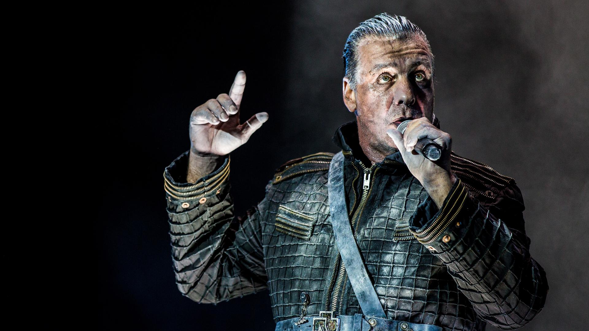 Das Foto zeigt den Sänger Till Lindemann. Er trägt eine Leder-Jacke und singt auf einer Bühne. 