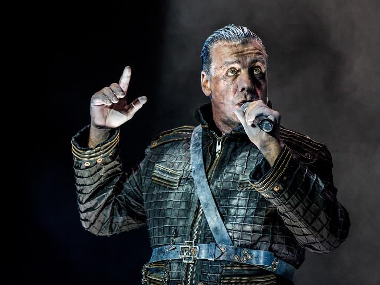 Till Lindemann trägt eine Lederjacke, steht auf einer Bühne und singt ins Mikrofon.