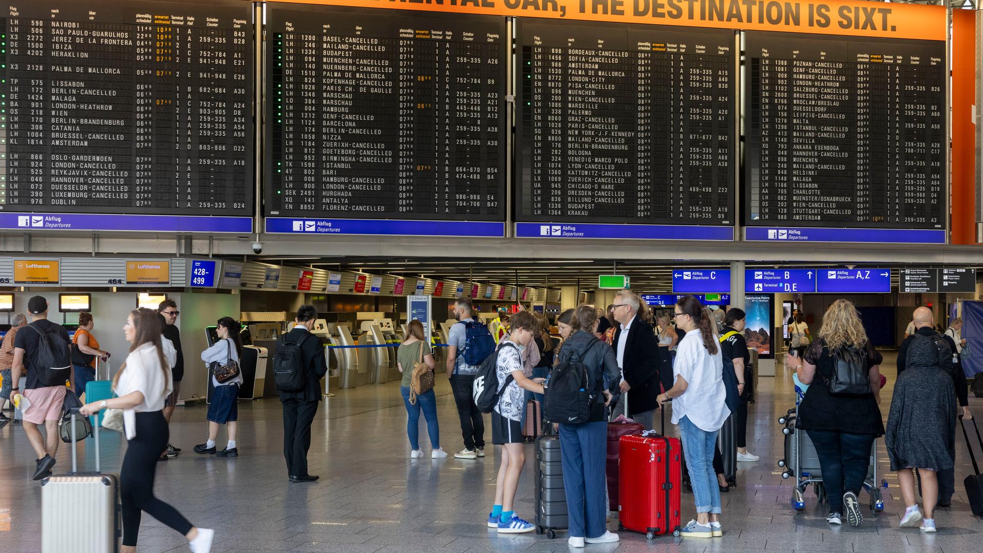 Frankfurt/Main: Reisende stehen im Terminal des Frankfurter Flughafens vor einer Anzeigetafel, auf der zahlreiche Abflüge gestrichen wurden.