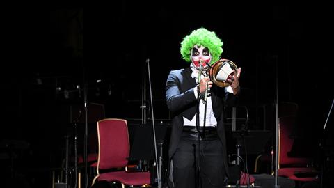 Ein als Clown geschminkter Posaunist hält den Dämpfer an sein Instrument und spielt