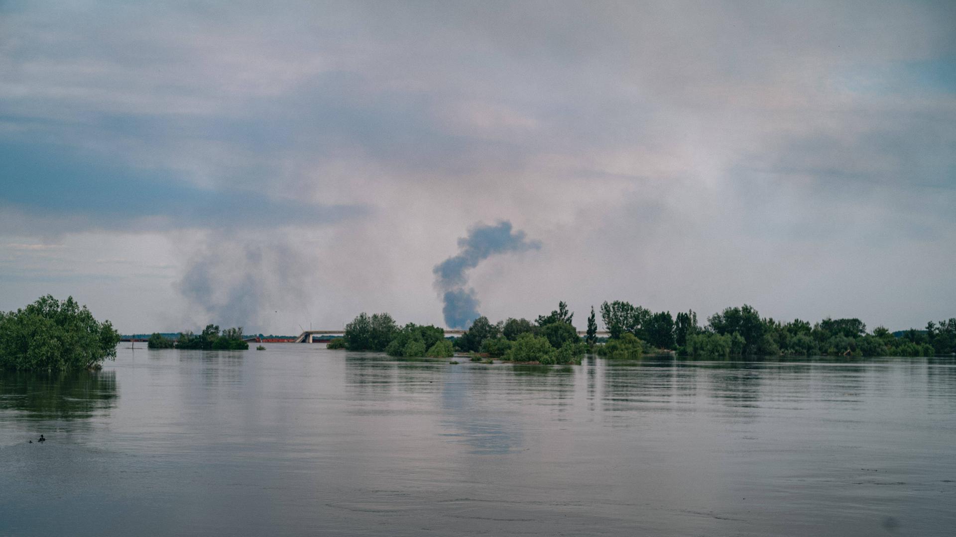 Ein Gebiet entlang des Dnipros, im Hintergrund liegen Teile einer zerstörten Brücke im Wasser.