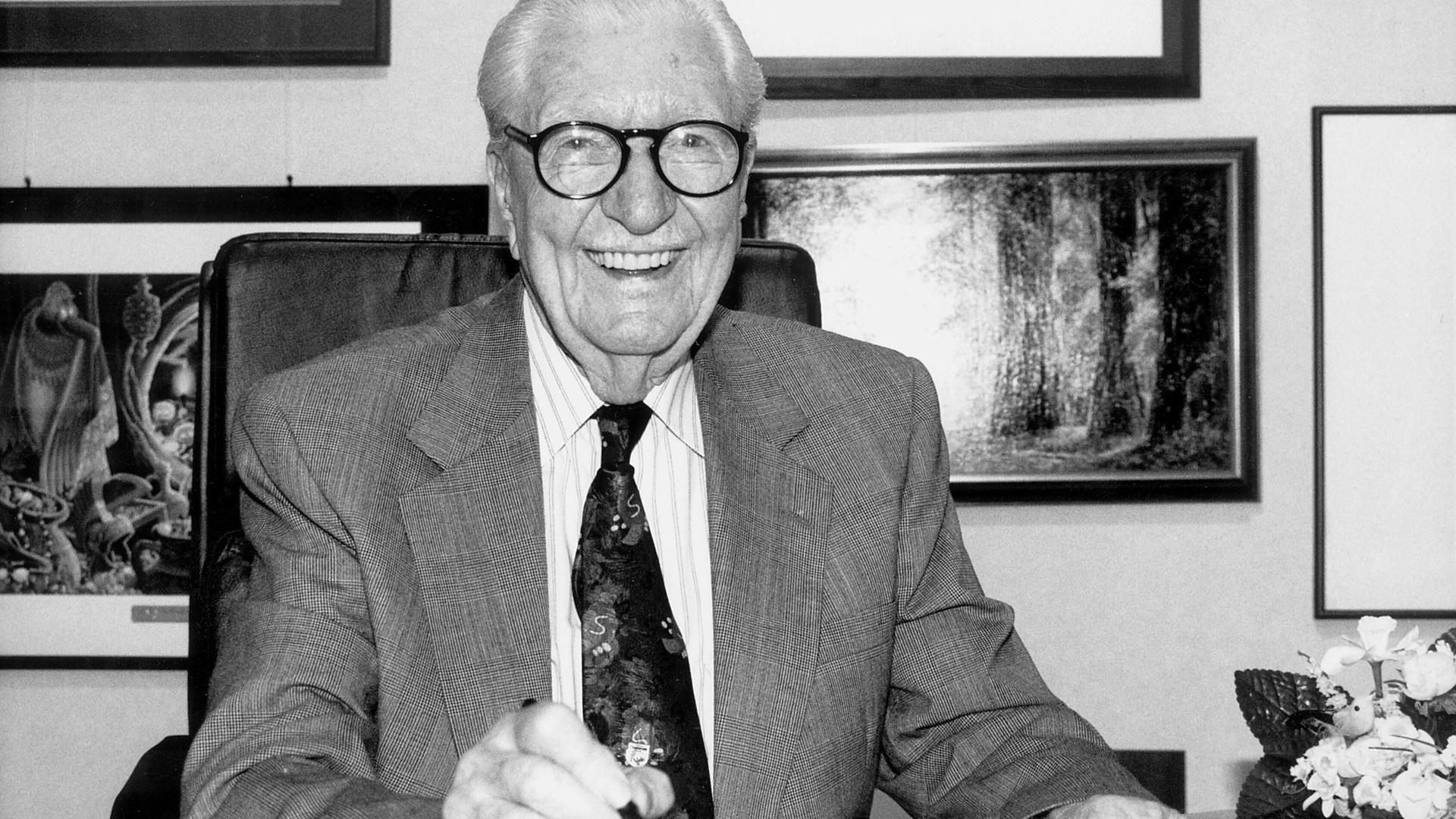 Das Schwarz-weiß-Foto zeigt Carl Barks, Zeichner der Donald-Duck-Figuren, lachend an einem Schreibtisch