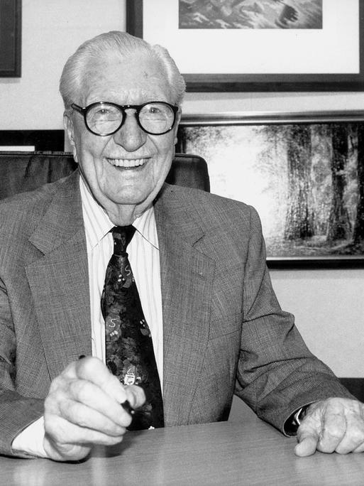 Das Schwarz-weiß-Foto zeigt Carl Barks, Zeichner der Donald-Duck-Figuren, lachend an einem Schreibtisch