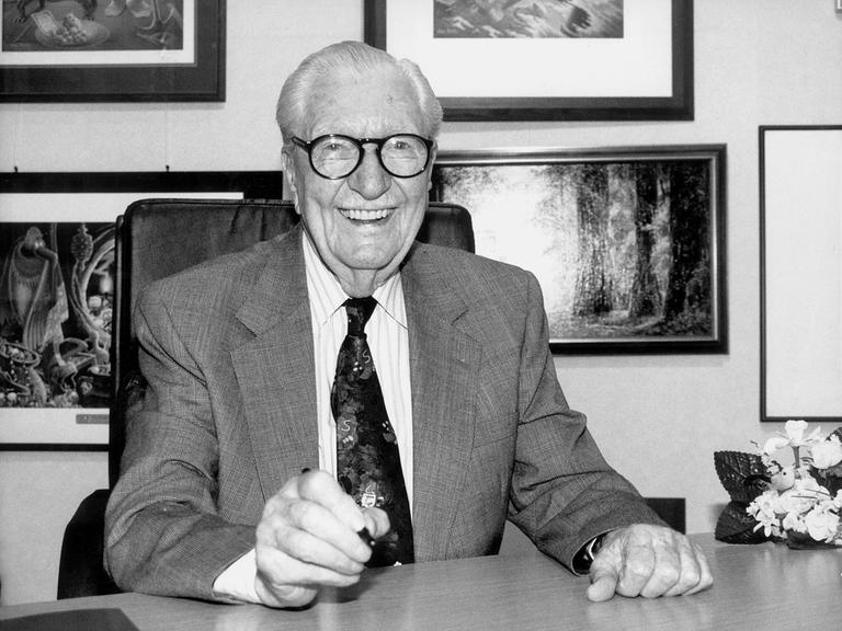 Das Schwarz-weiß-Foto zeigt Carl Barks, Zeichner der Donald-Duck-Figuren, lachend an einem Schreibtisch