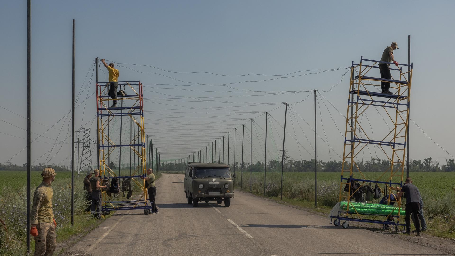 Ukrainische Arbeiter montieren Anti-Drohnen-Netze auf einer Straße. Ukrainische Arbeiter montieren Anti-Drohnen-Netze auf einer Straße.