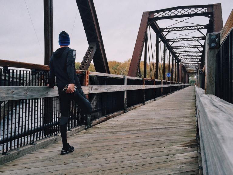Ein Jogger dehnt sich auf einer Brücke im Winter