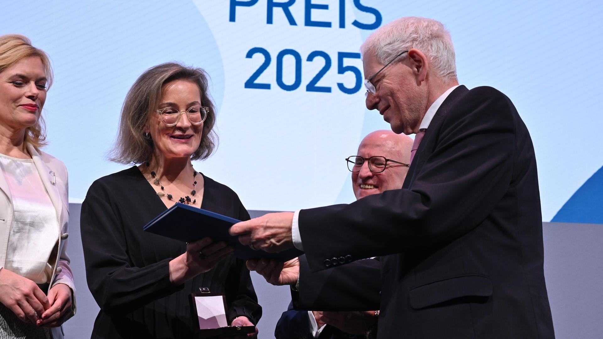 Die beiden stehen lächelnd nebeneinander. Links davon Bundestagspräsidentin Klöckner, dahinter ein ebenfalls lächeldner Mann. Alle stehen vor einer blauen Wand. 