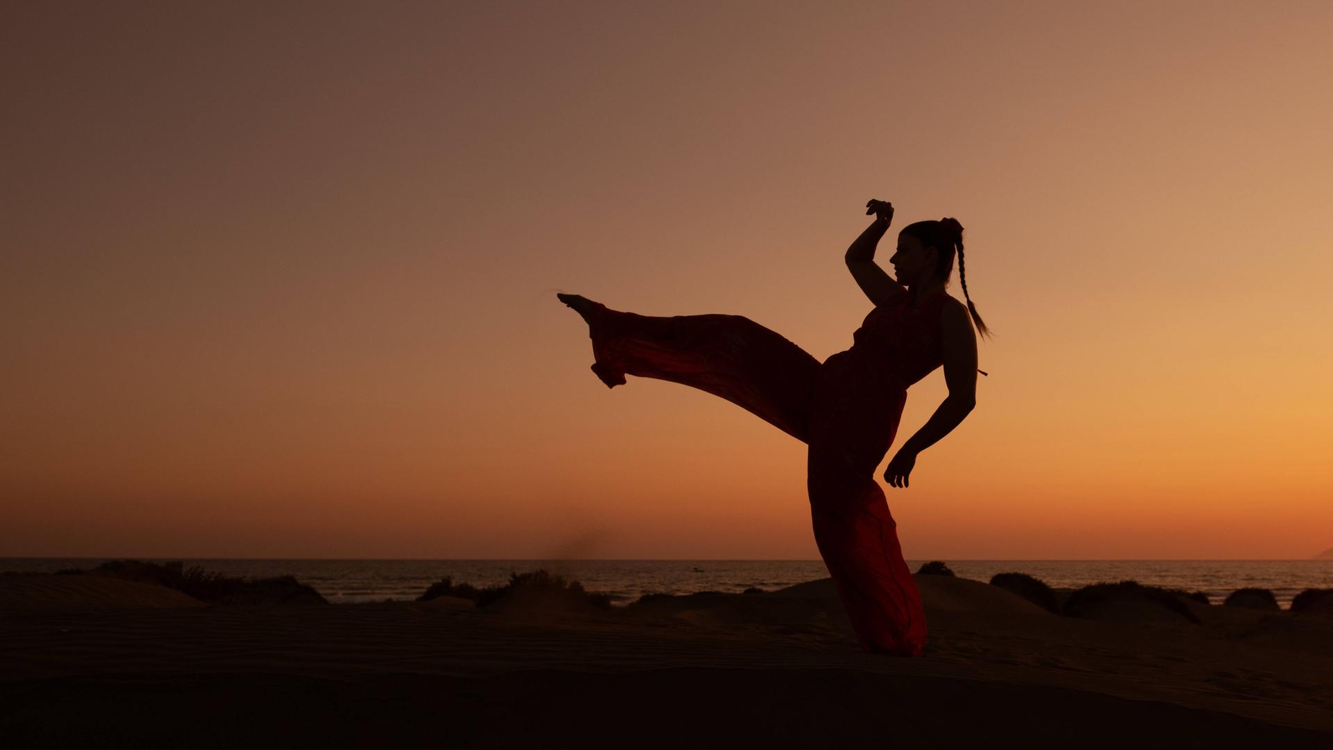 Eine Frau tanzt bei Sonnenuntergang am Strand - undatiertes Foto