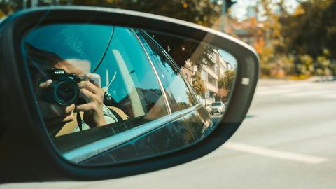In einem Autospiegel ist zu sehen, wie der Autofahrer ein Foto mit einer Kamera macht. In einem Autospiegel ist zu sehen, wie der Autofahrer ein Foto mit einer Kamera macht.