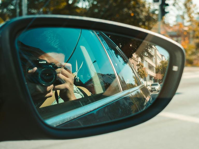 In einem Autospiegel ist zu sehen, wie der Autofahrer ein Foto mit einer Kamera macht.