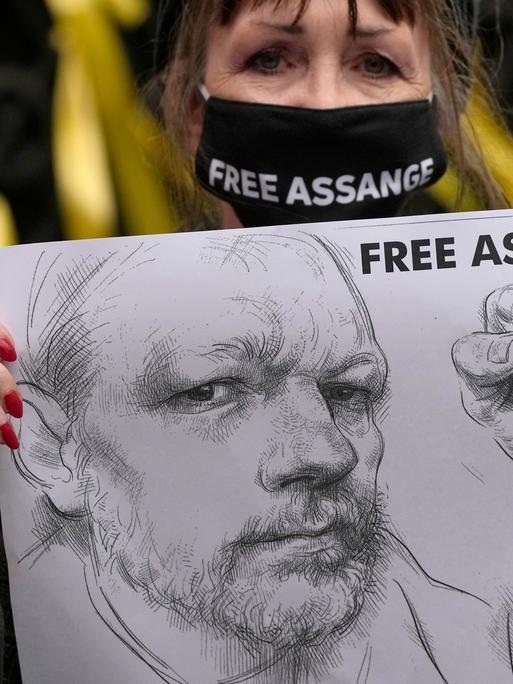 Vor dem High Court in London hält eine Unterstützerin mit Maske ein Plakat hoch. Zu sehen ist eine Bleistift-Zeichnung von Wikileaks-Gründer Julian Assange und die Forderung "FREE ASSANGE".
