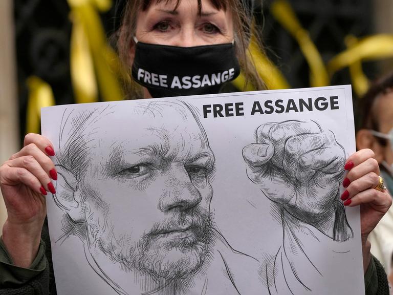 Vor dem High Court in London hält eine Unterstützerin mit Maske ein Plakat hoch. Zu sehen ist eine Bleistift-Zeichnung von Wikileaks-Gründer Julian Assange und die Forderung "FREE ASSANGE".