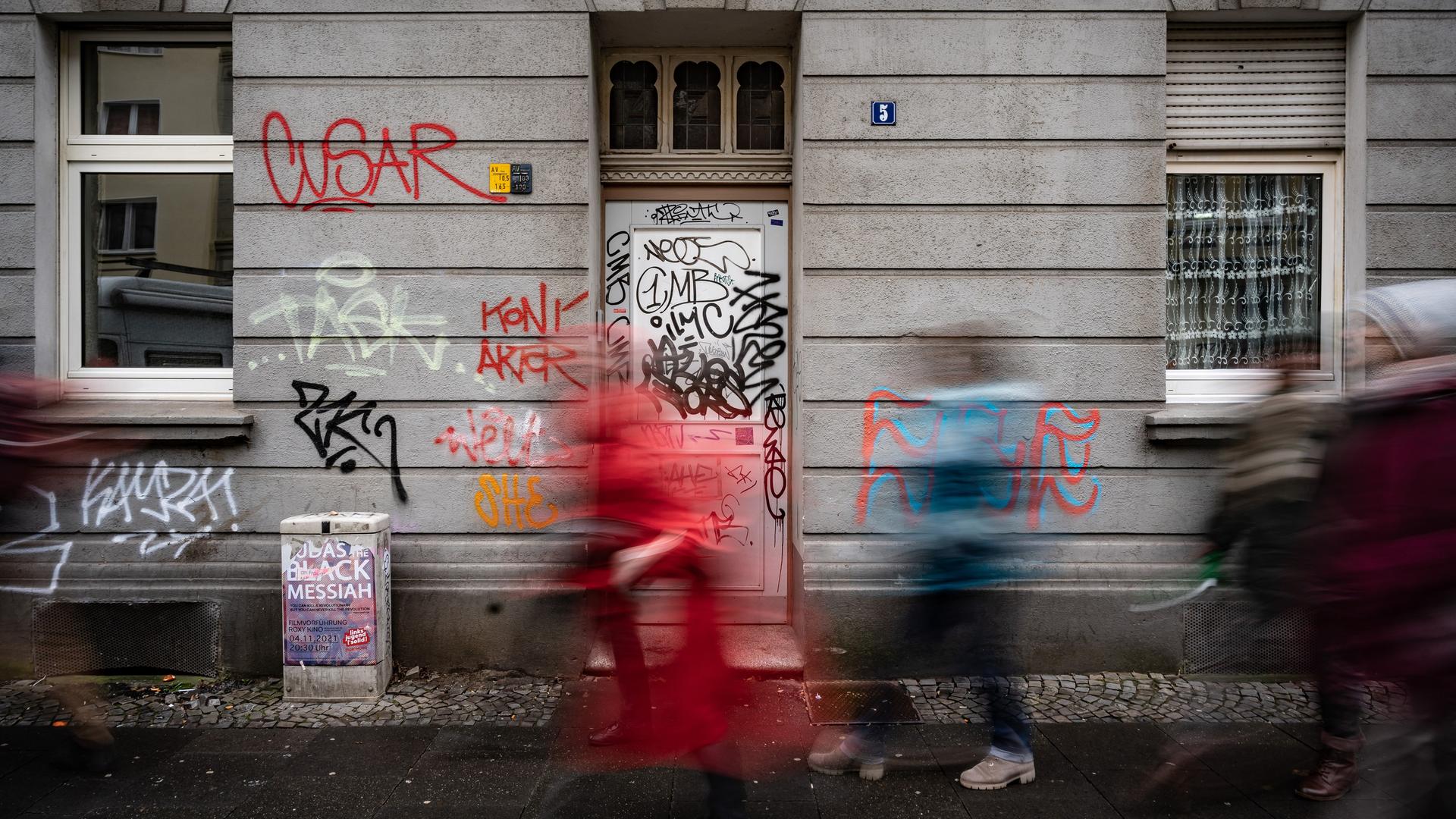 Drei Personen laufen vor einer mit Graffiti überzogenen Fassade in der Dortmunder Nordstadt vorbei.