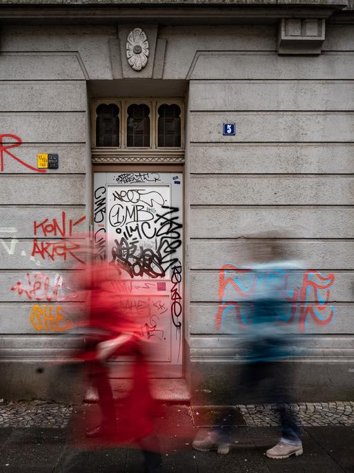 Drei Personen laufen vor einer mit Graffiti überzogenen Fassade in der Dortmunder Nordstadt vorbei.