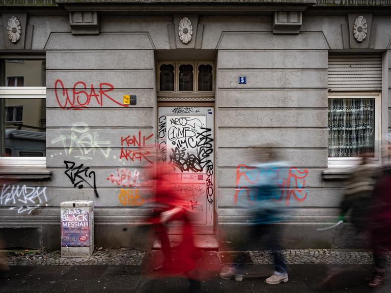 Drei Personen laufen vor einer mit Graffiti überzogenen Fassade in der Dortmunder Nordstadt vorbei.