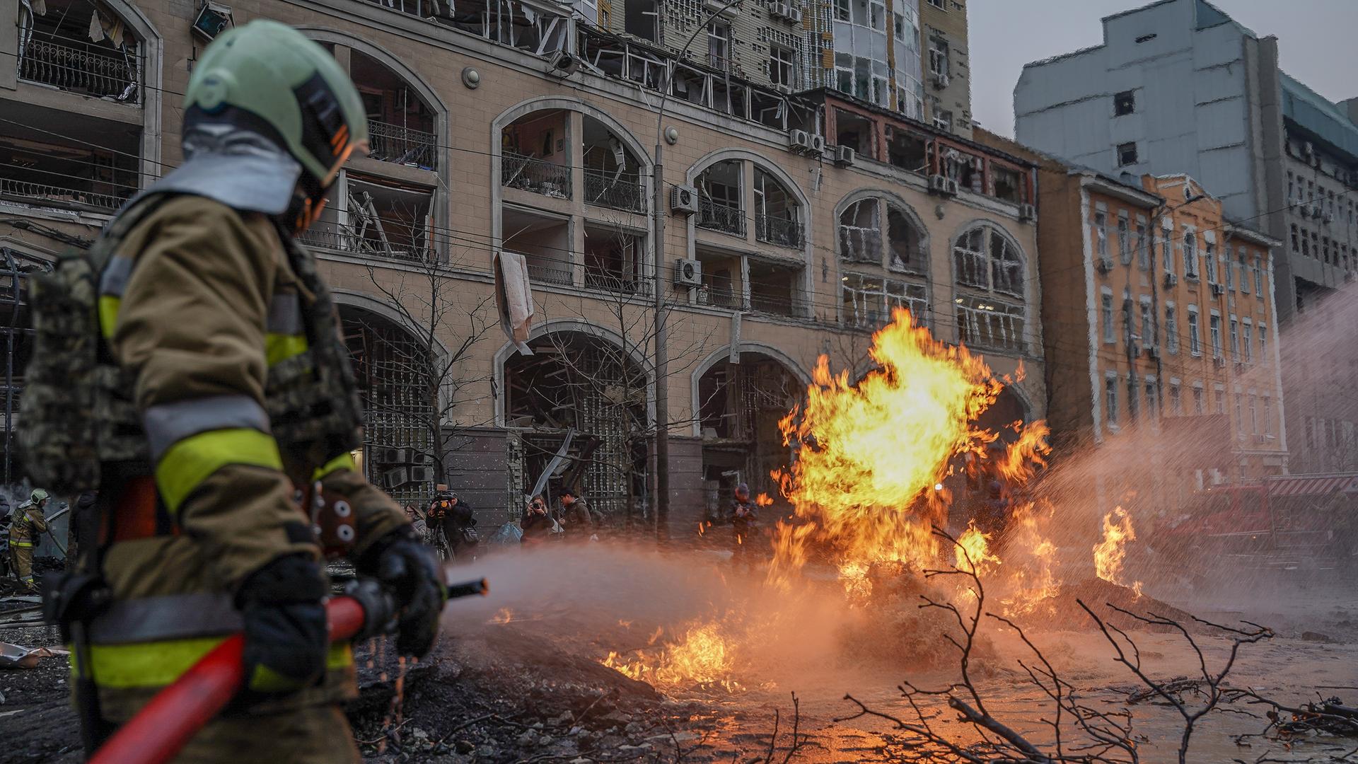 Ein Feuerwehrmann löscht einen Brand neben einem zerstörten Gebäude in Kiew. Ein Feuerwehrmann löscht einen Brand neben einem zerstörten Gebäude in Kiew.