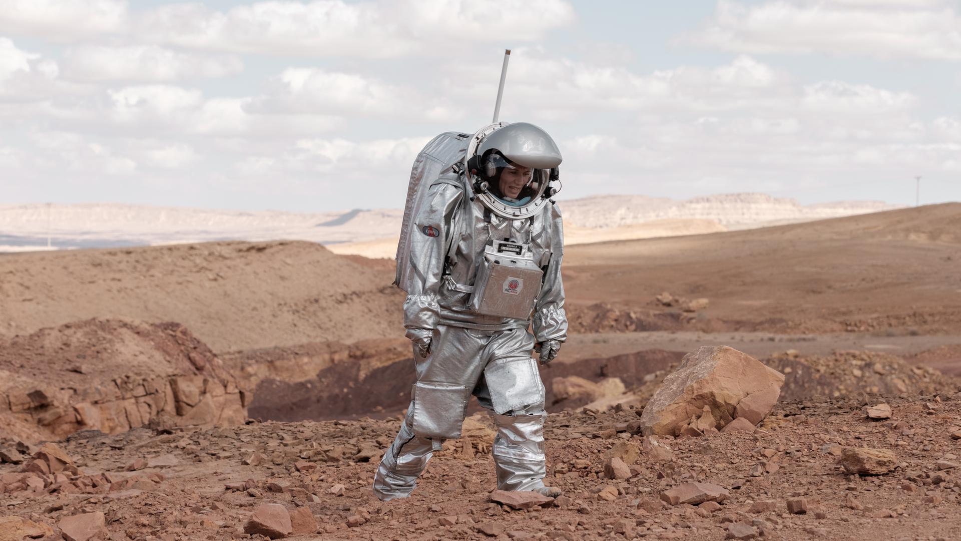 Foto der Analog-Astronautin Anika Mehlis, die in einem schweren, silbernen Raumanzug-Simulator im Rahmen einer Marsmission-Simulation durch die istraelische Negev-Wüste stapft Foto der Analog-Astronautin Anika Mehlis, die in einem schweren, silbernen Raumanzug-Simulator im Rahmen einer Marsmission-Simulation durch die istraelische Negev-Wüste stapft