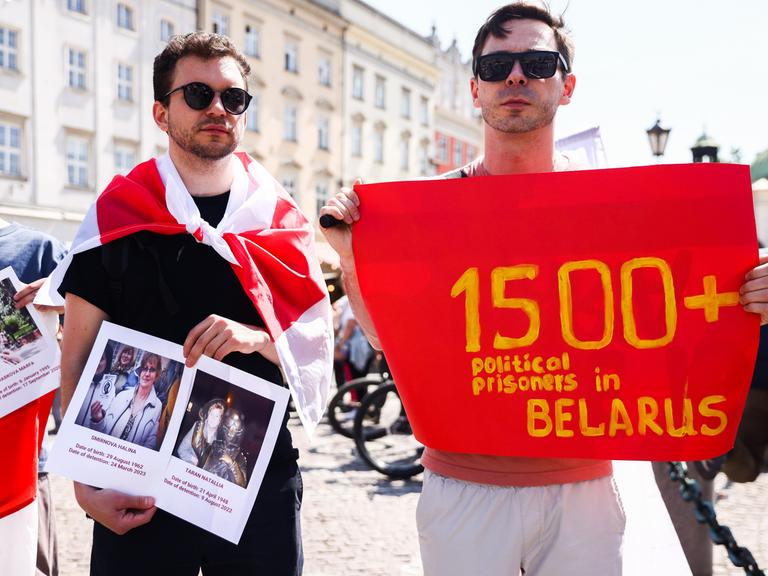 Zwei junge Männer halten Bilder politischer Gefangener und ein Banner, das auf mehr als 1500 politische Gefangene in Belarus verweisen soll.