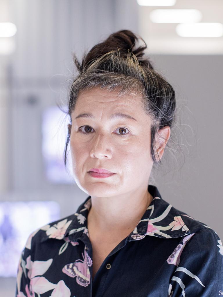 Portrait von Hito Steyerl, die in der Kunstsammlung K21 steht. Im Hintergrund sind im Raum aufgehängte Monitore zu sehen.
