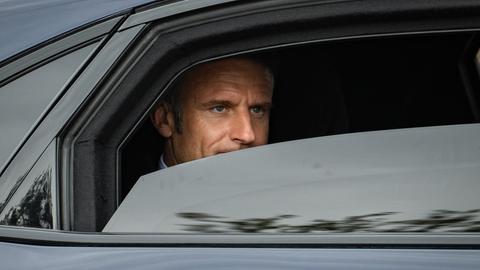 Frankreichs Präsident Emmanuel Macron sitzt in einer dunklen Limousine. Im halbgeöffneten Fenster ist sein Gesicht zu sehen.
