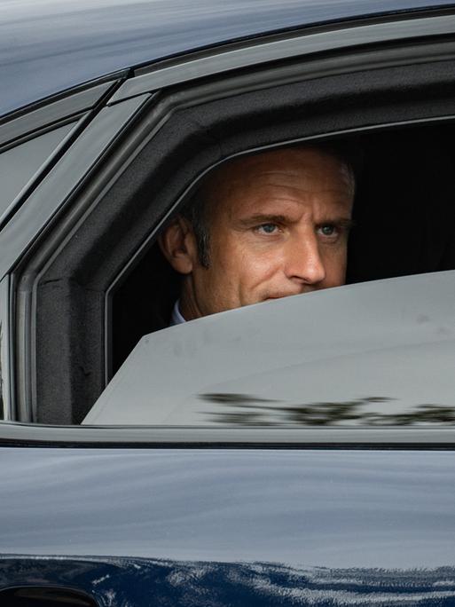 Frankreichs Präsident Emmanuel Macron sitzt in einer dunklen Limousine. Im halbgeöffneten Fenster ist sein Gesicht zu sehen.
