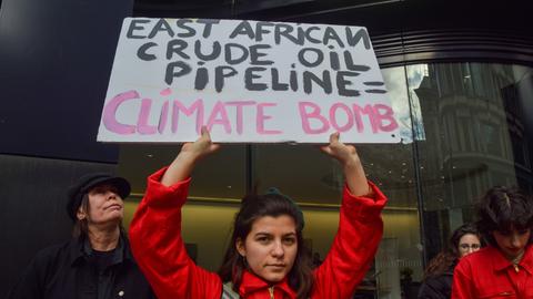 Eine junge Frau hält in London ein Schild in der Hand auf dem steht: "East African Crude Oil Pipeline = Climate Bomb". 