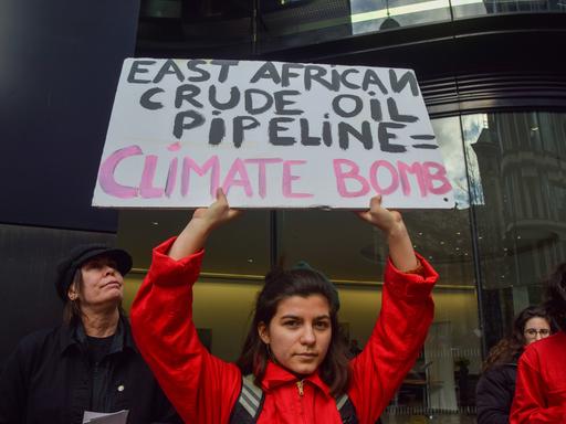 Eine junge Frau hält in London ein Schild in der Hand auf dem steht: "East African Crude Oil Pipeline = Climate Bomb". 