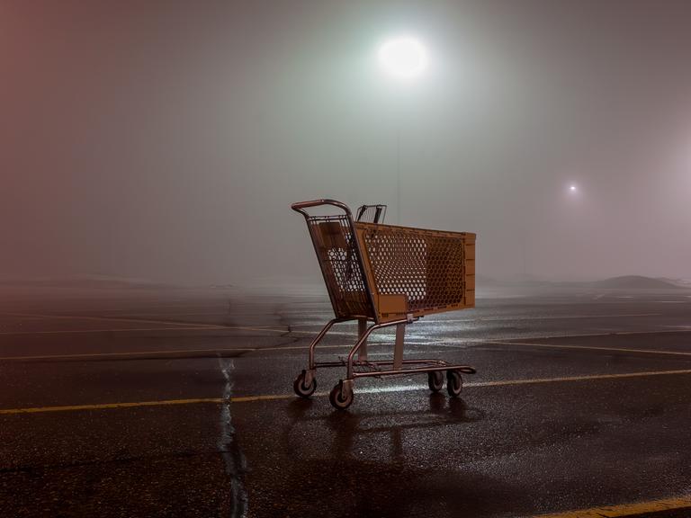 Ein leerer Einkaufswagen auf einem Parkplatz in der Dunkelheit.