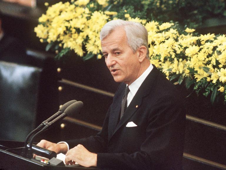 Der deutsche Bundespräsident Richard von Weizsäcker bei seiner vielbeachteten Rede im Bonner Bundestag am 8.5.1985 während der Feierstunde zum Ende des 2. Weltkrieges. Er steht im schwarzen Anzug vor einem gelben Blumenbouquet am Mikrofon. Der deutsche Bundespräsident Richard von Weizsäcker bei seiner vielbeachteten Rede im Bonner Bundestag am 8.5.1985 während der Feierstunde zum Ende des 2. Weltkrieges. Er steht im schwarzen Anzug vor einem gelben Blumenbouquet am Mikrofon.